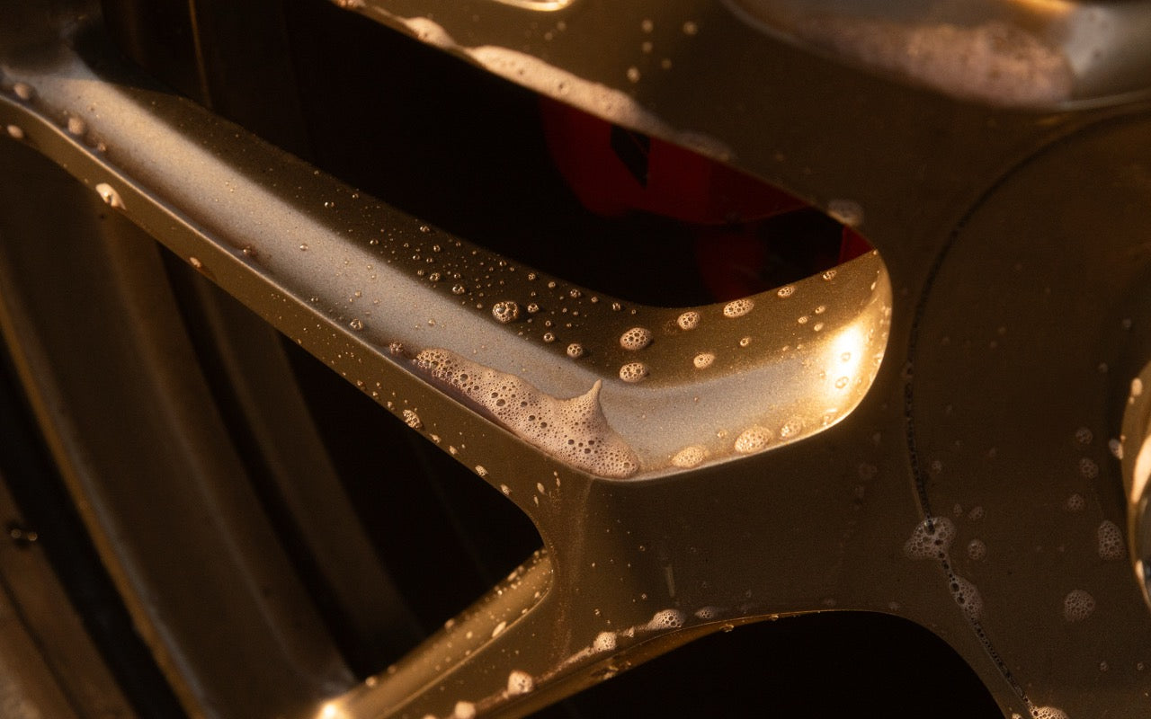 Foam and suds on gold alloy wheel spokes with a red brake caliper
