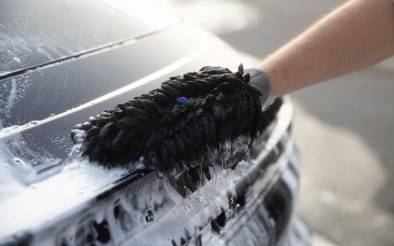 A wash mitt spreading thick foam across a dark car panel